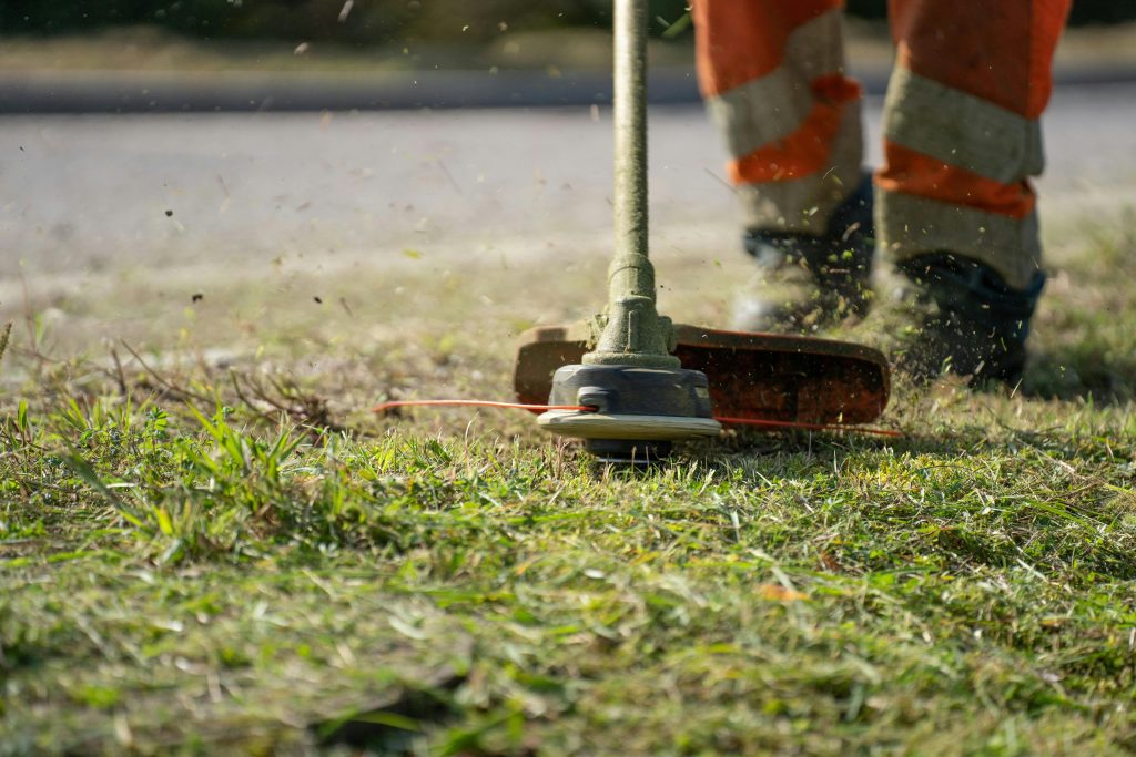 Close-up of a person trimming grass with a power tool outdoors.