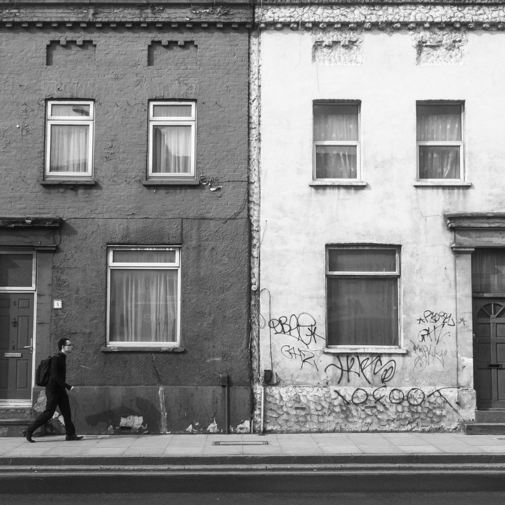 Monochrome photo of urban buildings with graffiti and a walking man on the sidewalk.